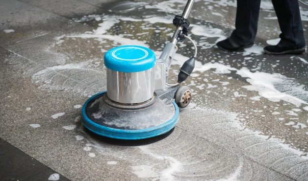 Professional deep cleaning service using an industrial floor scrubber machine to clean and sanitize tiled flooring with foam detergent.